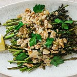 A white plate with roast air fryer asparagus topped with sliced almonds, capers, and fresh parsley leaves, served with a lemon wedge on the side—perfect for weeknight dinners as the best side dish.