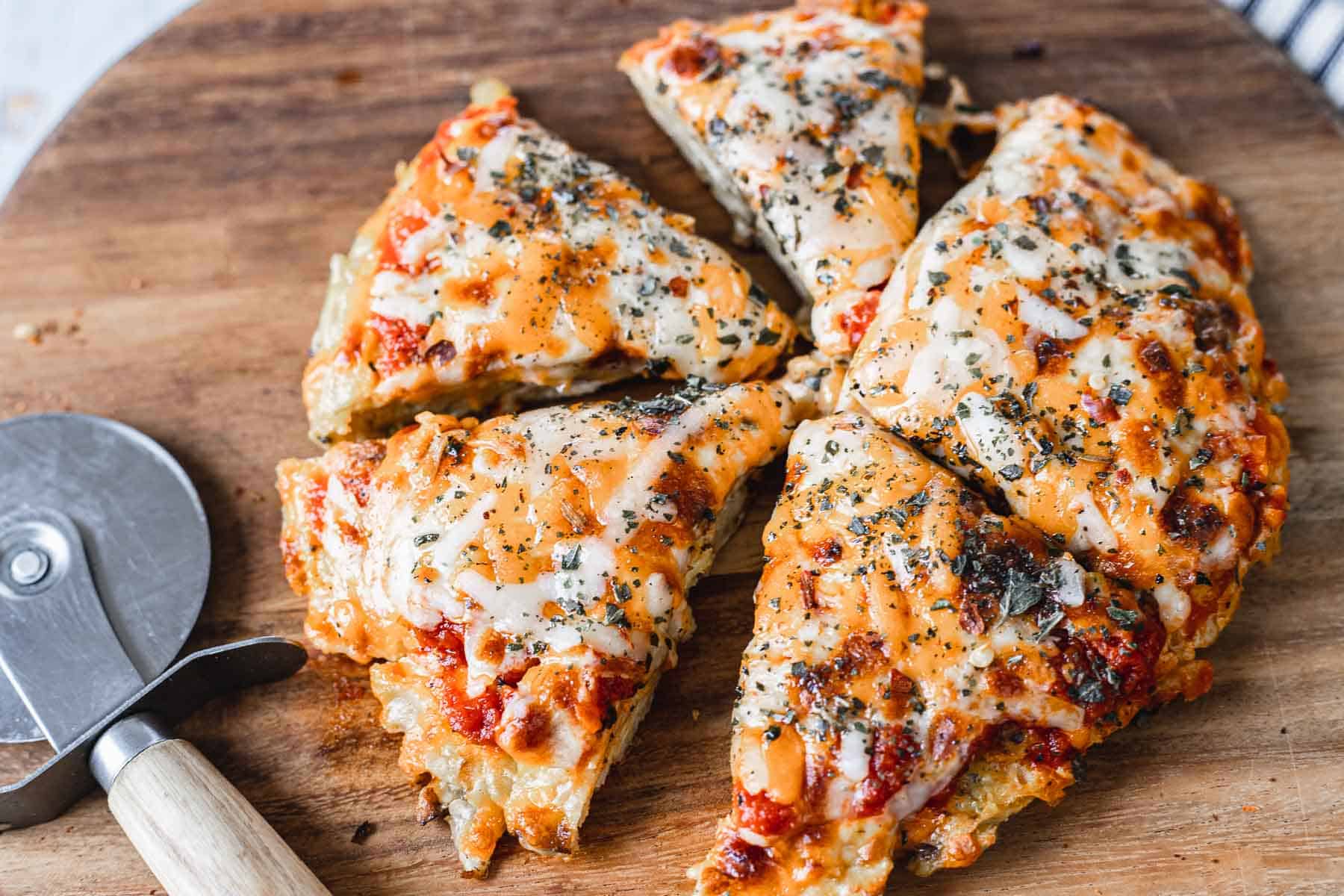 A round breakfast pizza cut into six slices sits on a wooden board, showcasing melted cheese, tomato sauce, and herbs. A metal pizza cutter is placed beside the tempting creation, inviting you to discover how to make a breakfast pizza masterpiece like this.