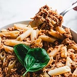 A close-up of a bowl of chicken marinara pasta with shredded chicken and sauce. A fork lifts a portion, showcasing the easy weeknight delight. A fresh basil leaf crowns the dish, adding a touch of elegance.