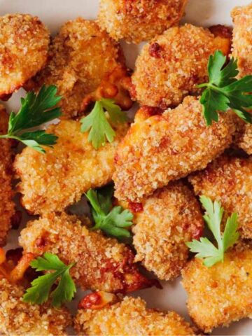 A plate of breaded chicken nuggets garnished with parsley. The nuggets are golden brown, and the dish is placed on a white surface with a striped cloth partially visible.