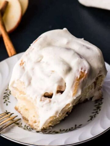 A pan of freshly baked and frosted apple cinnamon rolls on a dark blue background.