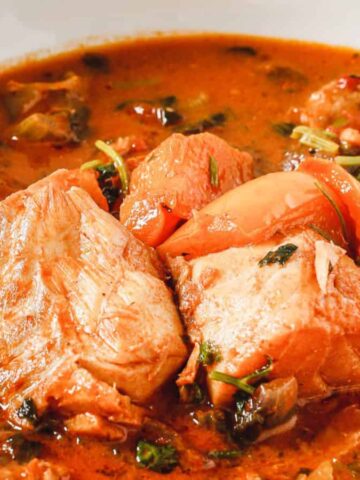 A close-up of a bowl of fish stew with chunks of fish, tomatoes, and herbs in a rich, red broth.