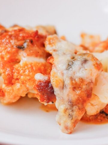 A serving of lasagna with layers of pasta, cheese, and tomato sauce is placed on a white plate. The dish has a golden-brown crust and appears to be freshly baked.