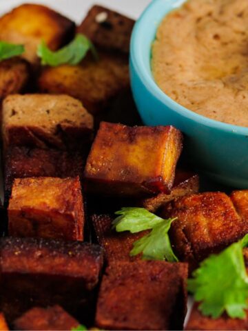 A plate of crispy tofu cubes garnished with cilantro is placed next to a small bowl of creamy dipping sauce in a blue dish.