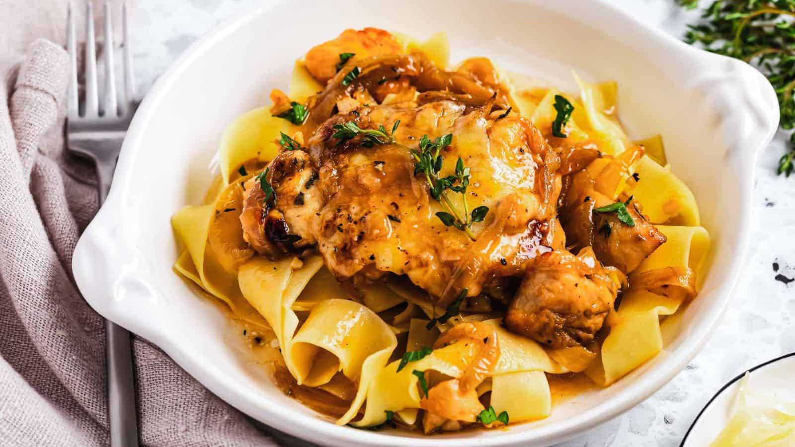 A close-up of a baked dish in a skillet featuring melted cheese, onions, and herbs. A serving spoon is lifting a portion, highlighting the golden-brown cheese and caramelized onions on top.
