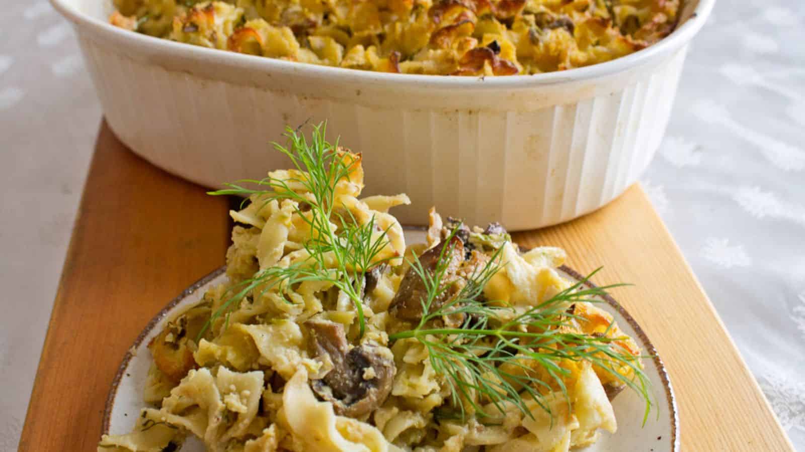 A white dish filled with creamy pasta topped with mushrooms and herbs is placed on a blue and white striped cloth.
