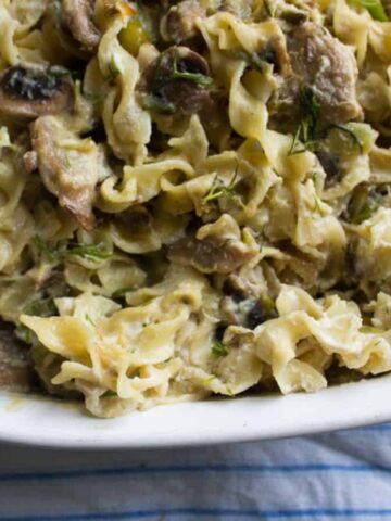 A close-up of a comforting dish filled with creamy mushroom pasta. The pasta is tossed with sauce, mushrooms, and garnished with fresh herbs, evoking the warmth of Grandma's Kitchen. The dish is placed on a blue and white striped cloth.