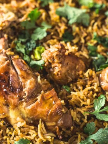 A close-up of comforting biryani in a large dish, featuring spiced chicken mixed with fragrant basmati rice. Reminiscent of Grandma's kitchen, the dish is garnished with fresh cilantro leaves.