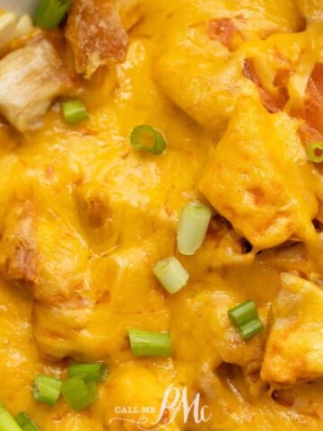 A close-up of a cheesy dish topped with chopped green onions. The dish appears to have chunks of meat and a thick layer of melted cheese, giving it a rich and hearty appearance.