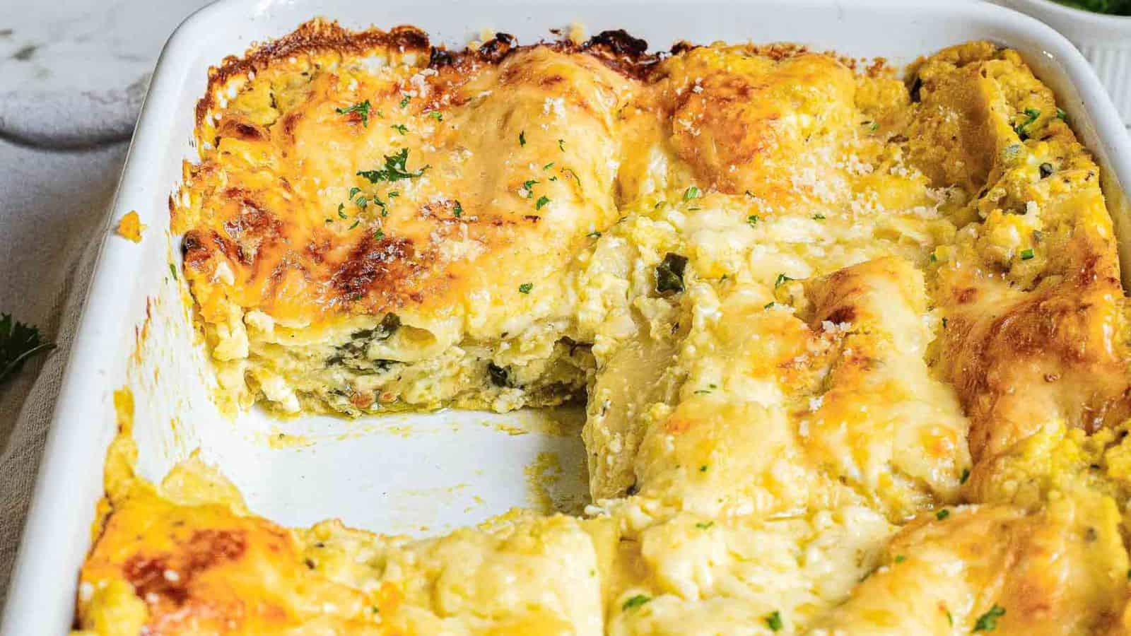 A baked dish of zucchini lasagna with a golden-brown cheese topping. A wooden spatula lifts a square piece, revealing layers of zucchini, cheese, and spinach. The casserole dish is partly cut, showing more servings. Garnished with herbs.