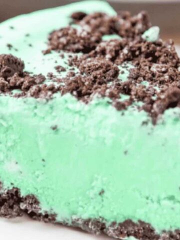 A slice of mint chocolate pie on a white plate. The pie features a smooth, green mint-flavored filling topped with crushed chocolate cookie pieces, and a chocolate cookie crust.