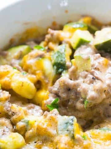 A close-up of a comforting casserole in a bowl, featuring ground meat, diced zucchini, and melted cheese. A spoon rests in the bowl, ready to serve. The dish is garnished with chopped parsley, making you feel at home with every bite.