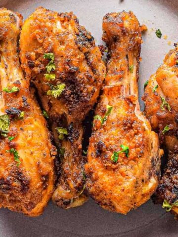 Four seasoned and grilled chicken drumsticks, crafted from the finest air fryer recipes, are garnished with chopped herbs and arranged on a gray plate. Fry without the guilt!