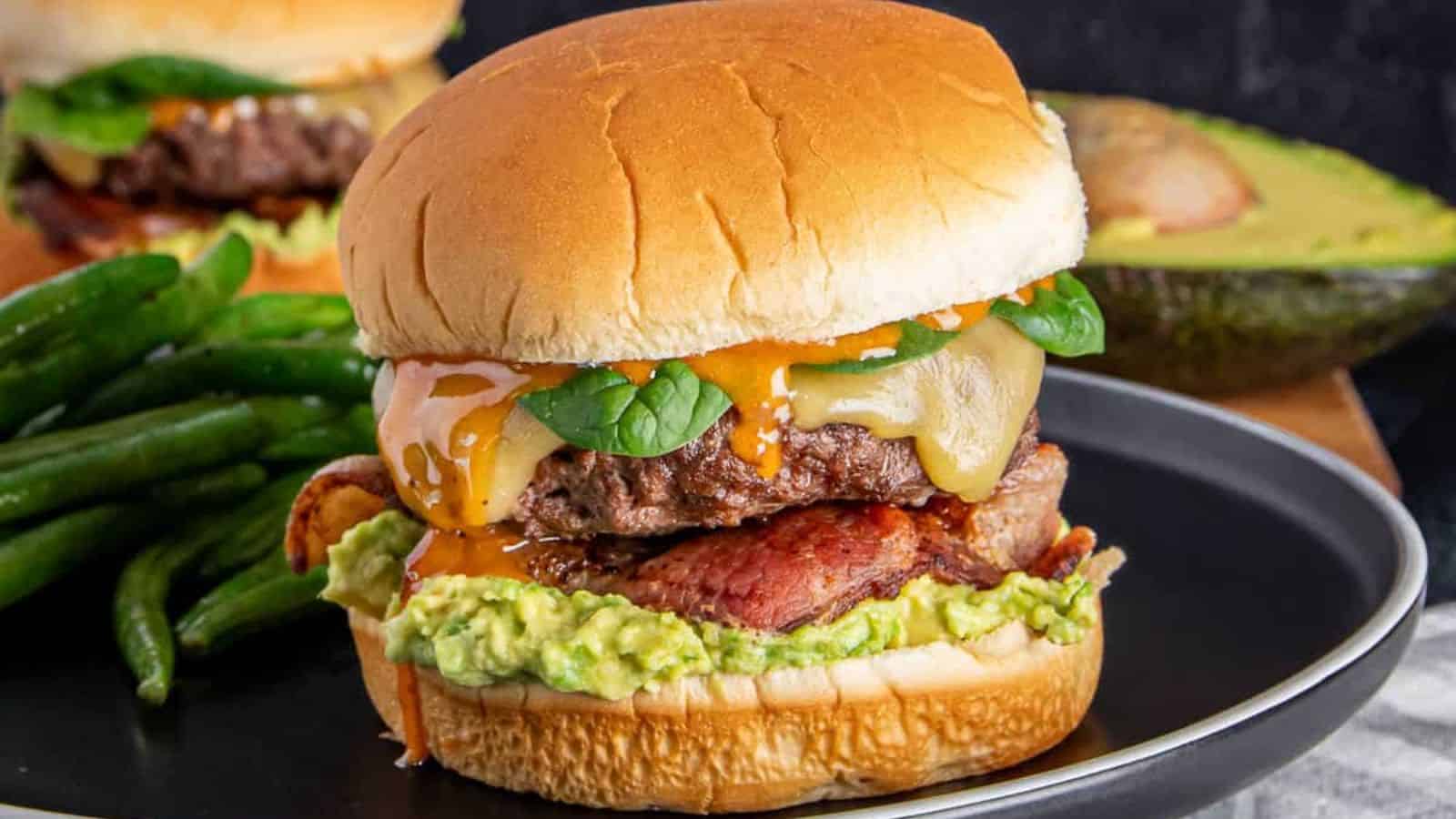 An up-close shot of bacon-avocado ground beef burger on a flat white surface.