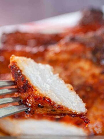 A fork holds a slice of grilled, seasoned meat with a charred exterior, promising a flavorful bite. In the background, more pieces of this tender delight await on the plate. Try tonight for an effortless meal; it's one of those simple recipes that'll make your dining experience truly special.
