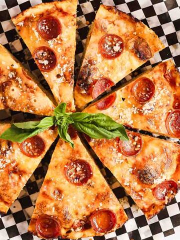 Sliced pepperoni pizza on a checkered platter garnished with fresh basil.