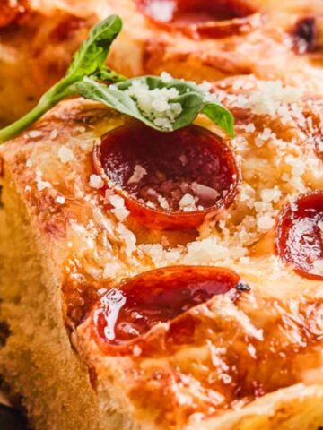 Close-up of cheesy pepperoni pizza with a garnish of fresh basil.