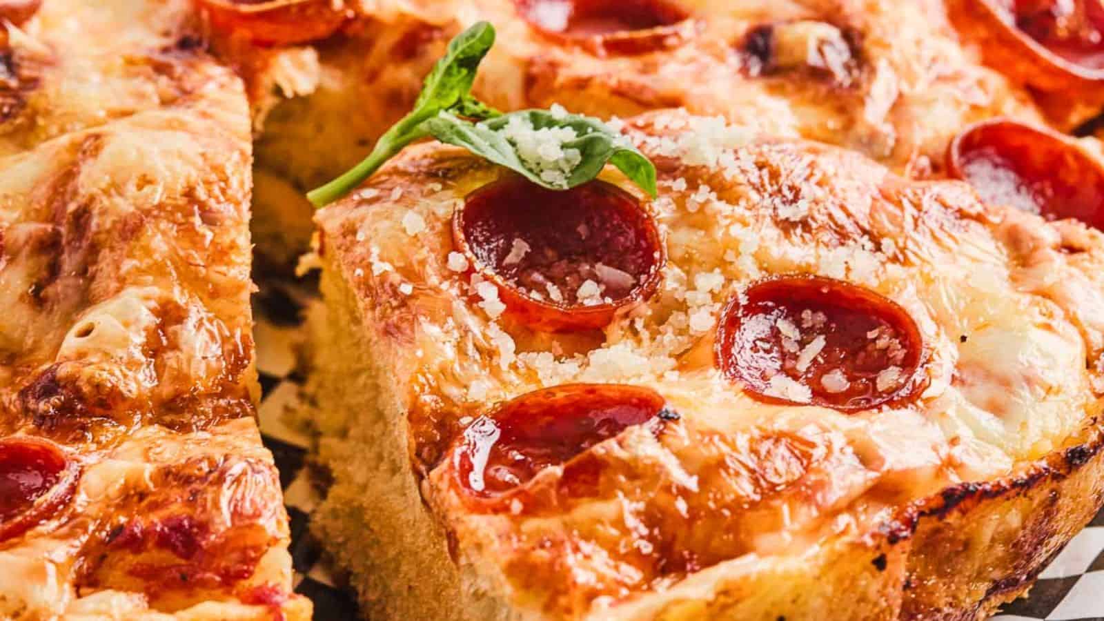 Sliced pepperoni pizza on a checkered platter garnished with fresh basil.