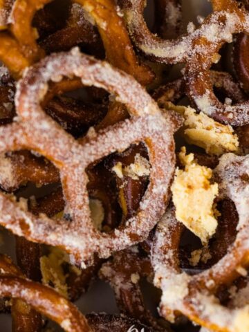 Close-up image of salted pretzels. The pretzels are golden brown and lightly coated with salt, arranged in a scattered manner. Some crumbs are visible among the pretzels, indicating a crunchy texture.