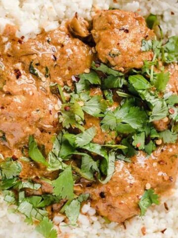A bowl of cauliflower rice topped with a creamy tomato-based curry and garnished with fresh cilantro. The dish is served in a white bowl on a white surface.