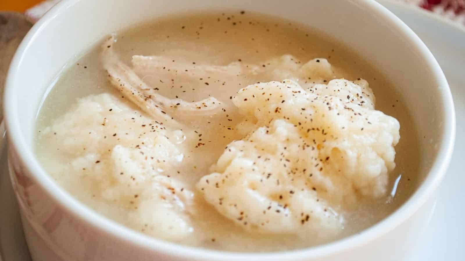 Soft dumplings in a white bowl with chicken and black pepper.
