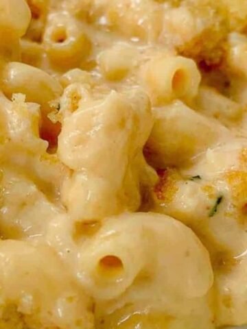 Close-up image of a creamy macaroni and cheese topped with a golden, crispy breadcrumb crust. This winter comfort dish appears rich and cheesy, with visible pasta shapes coated in the luscious sauce on a white plate.