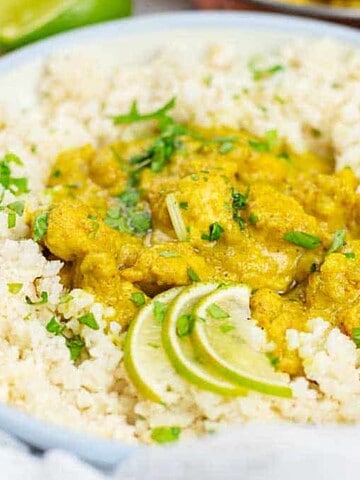 A plate of rice topped with a yellow curry dish, garnished with fresh cilantro for a stress-free dinner idea everyone will love. Two lime wedges are placed on the side, all set on a light-colored table surface.