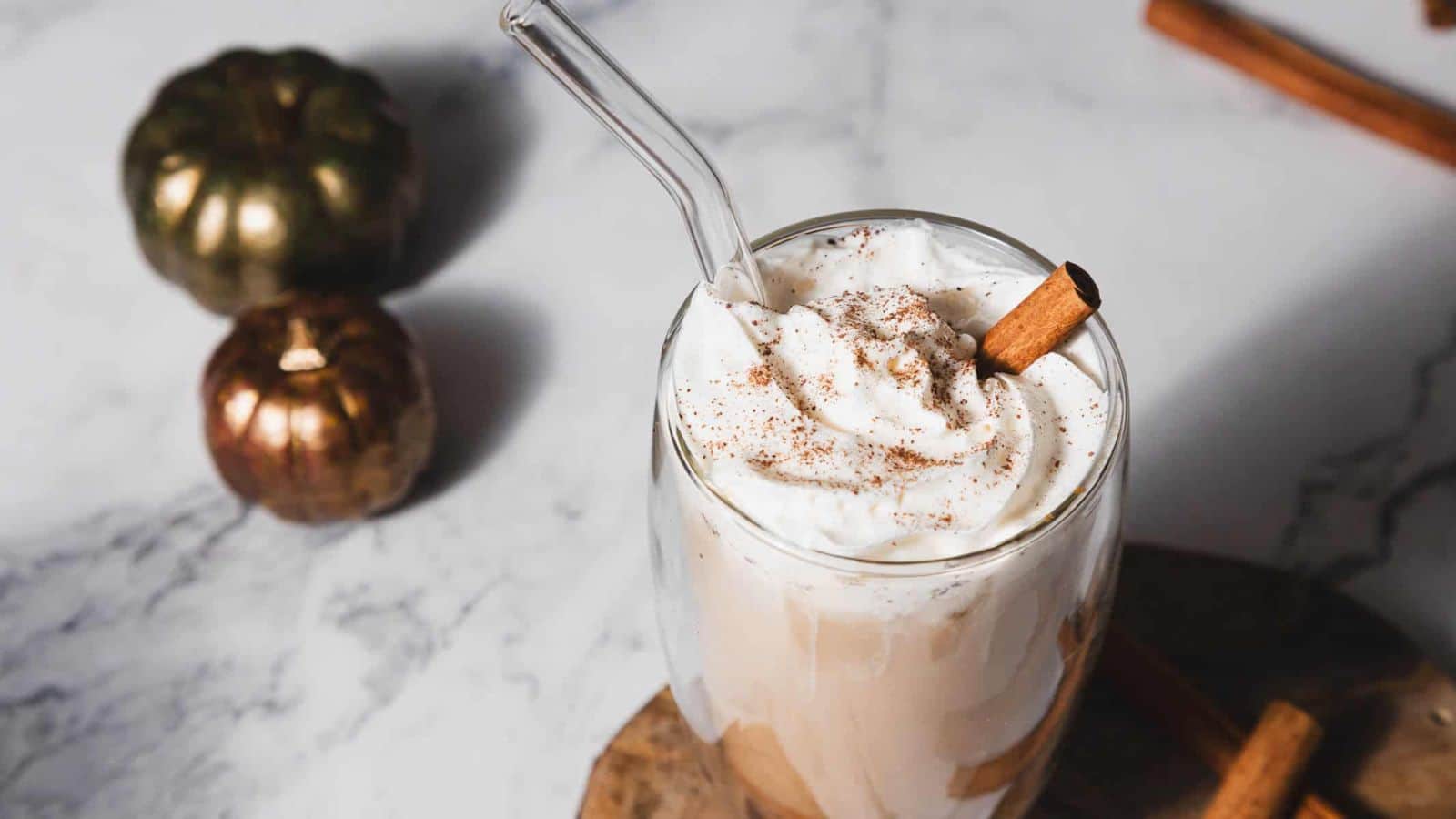 A pumpkin spice cold brew in a glass, topped with whipped cream and a cinnamon stick, with decorative elements in the background.