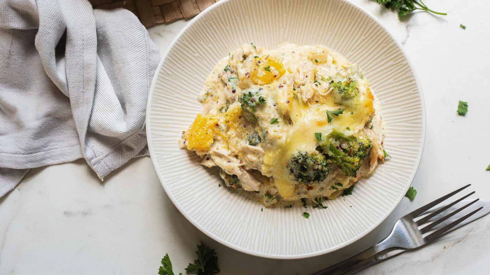 A baked casserole dish containing a cheesy broccoli and chicken mixture, topped with pieces of pineapple and sprinkled with chopped parsley.