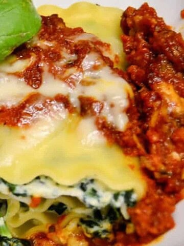 Two servings of rolled lasagna are topped with a thick layer of red sauce, ideal for hearty meals. The pasta is stuffed with a spinach and cheese filling, making it perfect for big gatherings. A fresh basil leaf is placed on top as a garnish.