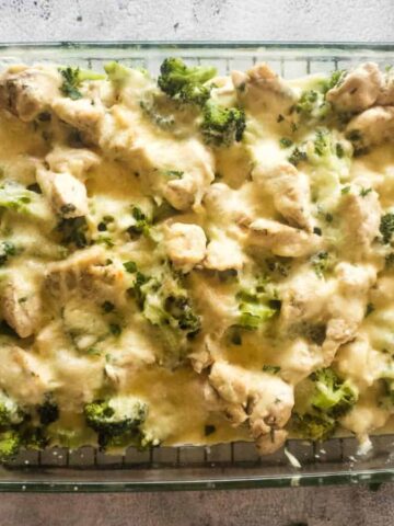 A glass baking dish containing a delicious casserole with chicken pieces, broccoli florets, and melted cheese on top. The dish is placed on a wire rack over a textured gray surface.