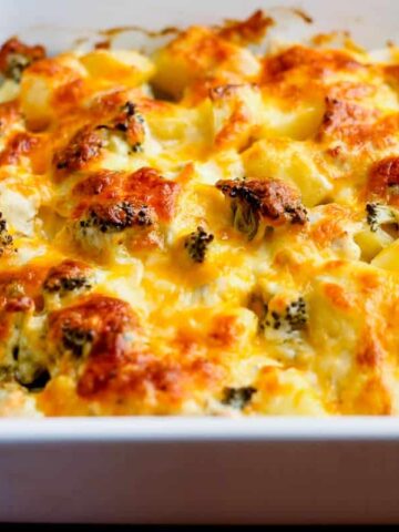 A white baking dish holds a comforting winter casserole, topped with golden-brown cheese. Visible ingredients include broccoli florets and chunks of potatoes, all baked to perfection with melted cheese, creating a crispy layer that's sure to warm up your favorite winter recipes.