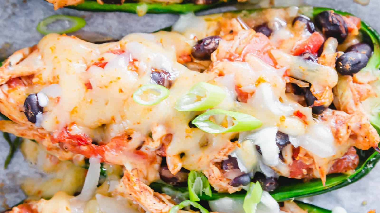 Close-up of a dish featuring oven-baked jalape&ntilde;os filled with melted cheese, black beans, diced tomatoes, and chicken. Green onion slices sprinkle the top as garnish. Perfect as a cozy dinner idea, the melted cheese offers a smooth and gooey texture.