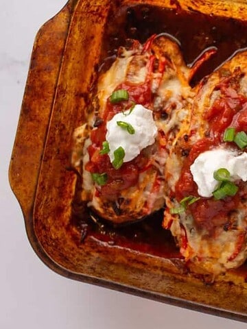 Baked stuffed bell peppers filled with melted cheese and topped with dollops of sour cream, salsa, and chopped green onions, arranged in a glass baking dish on a white surface.