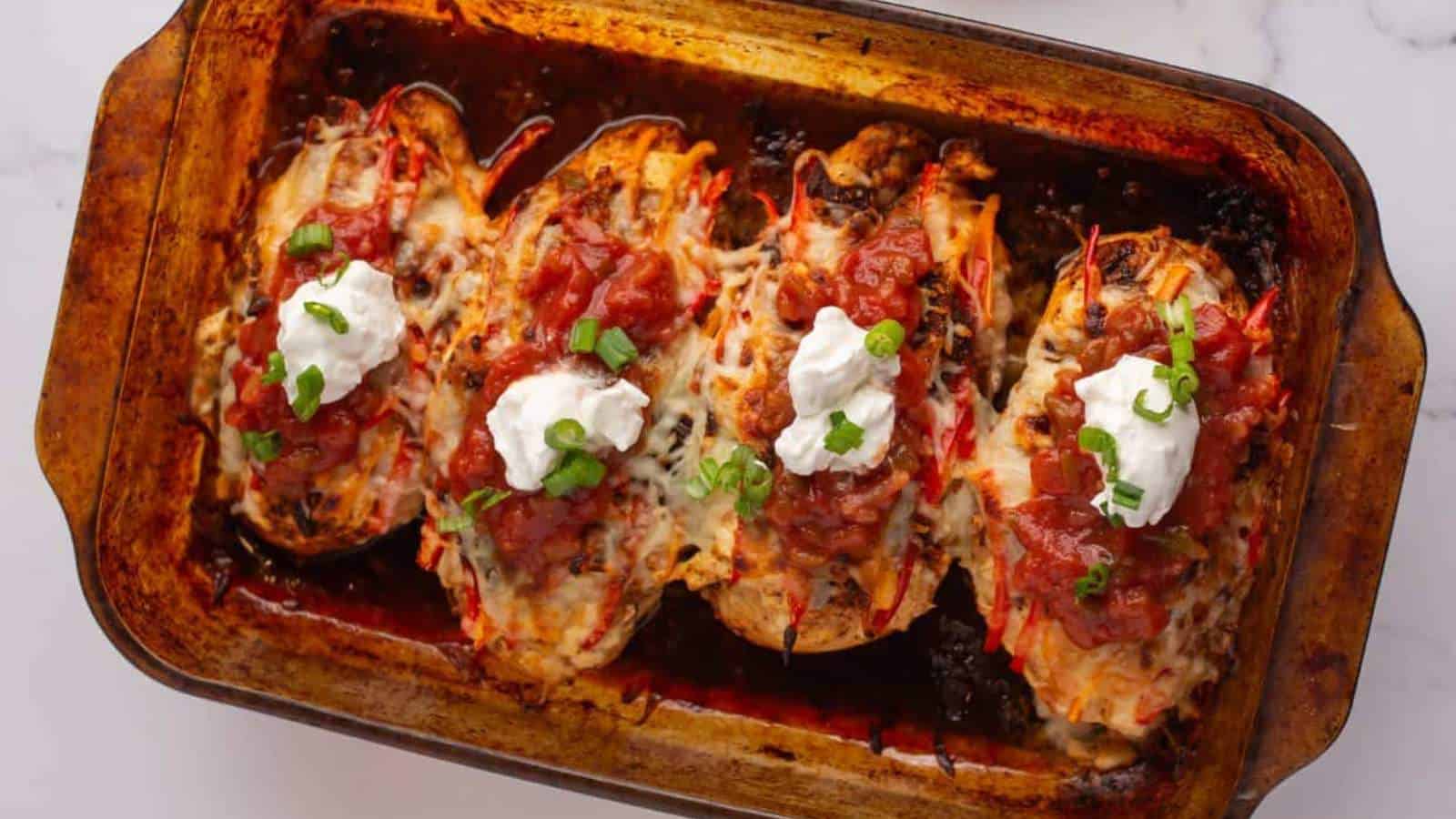 Baked stuffed bell peppers filled with melted cheese and topped with dollops of sour cream, salsa, and chopped green onions, arranged in a glass baking dish on a white surface.