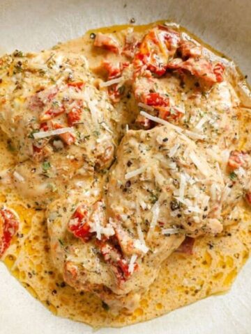 A skillet of creamy sun dried tomato chicken with a wooden spoon.