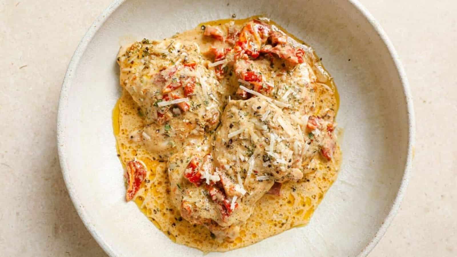 A skillet of creamy sun dried tomato chicken with a wooden spoon.