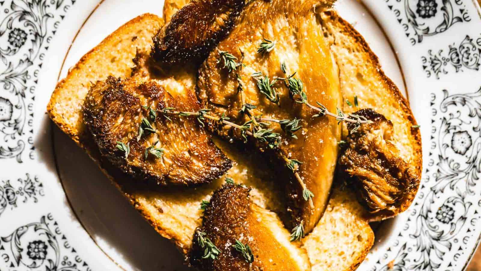 Close-up of a piece of toast topped with caramelized mushrooms and sprigs of fresh thyme. The lighting highlights the golden-brown color and texture of the mushrooms. The scene is set on a white plate with a decorative rim.