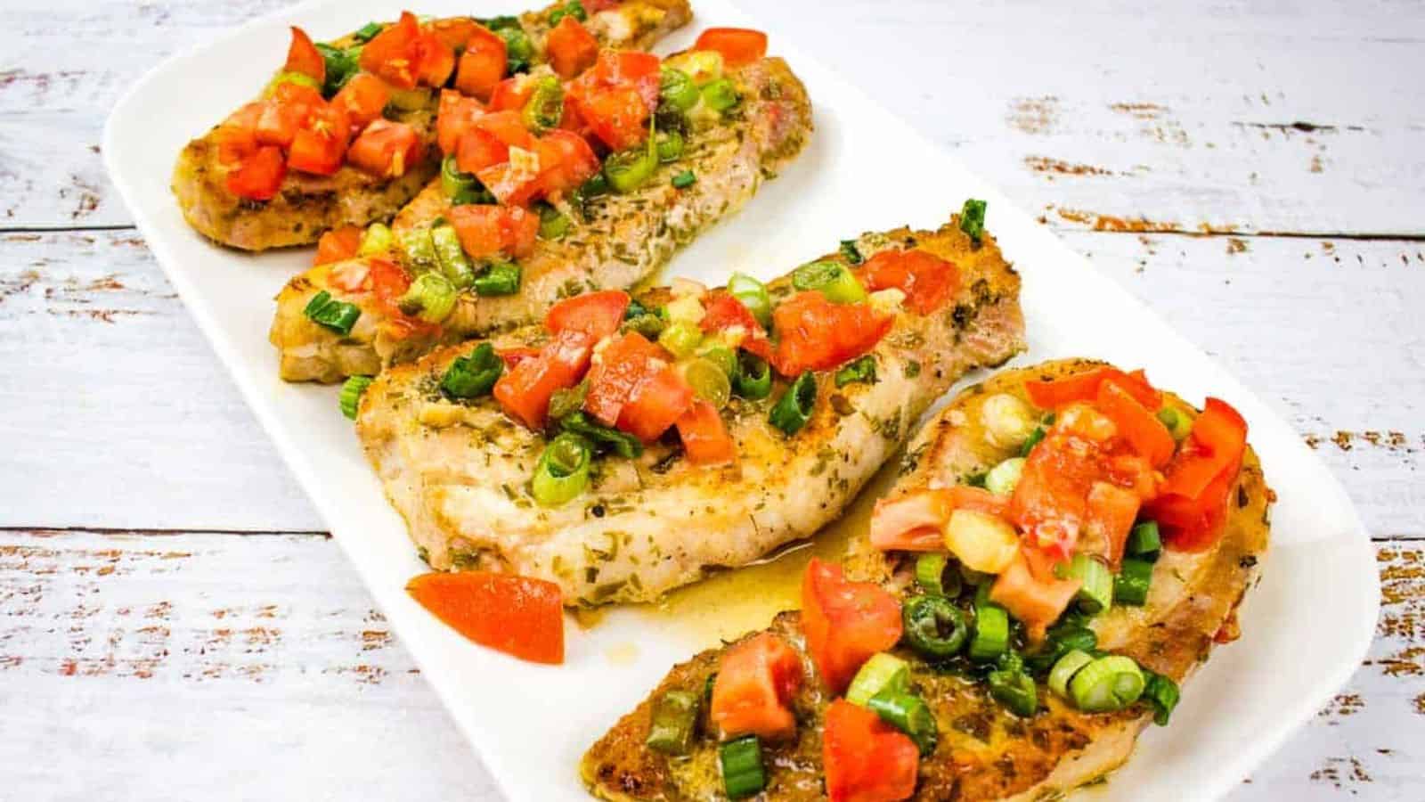 Three pork chops with tomato and green onion on a white plate.
