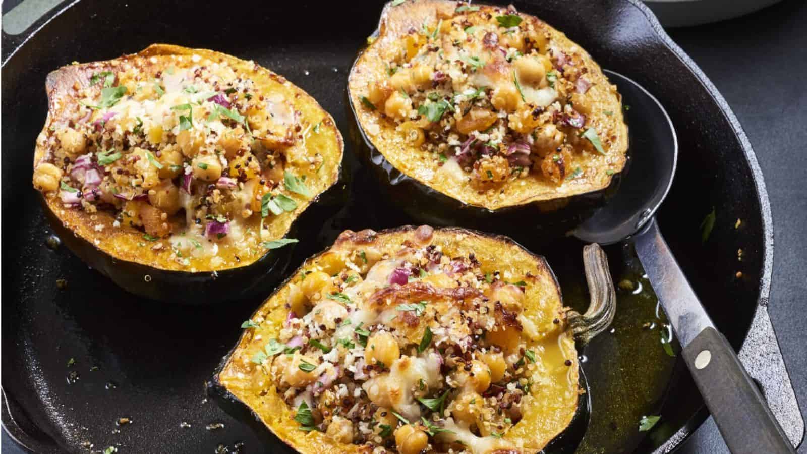 A cast iron skillet holds three halves of roasted acorn squash filled with a stress-free mixture of chickpeas, quinoa, herbs, and melted cheese. Perfect for impressing in-laws, a serving spoon rests on the skillet's edge.