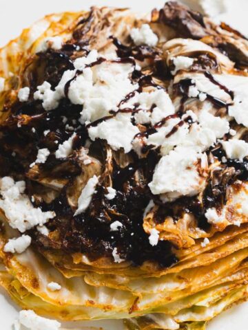 A stack of crepes topped with crumbled feta cheese and drizzled with balsamic glaze, served on a white plate.