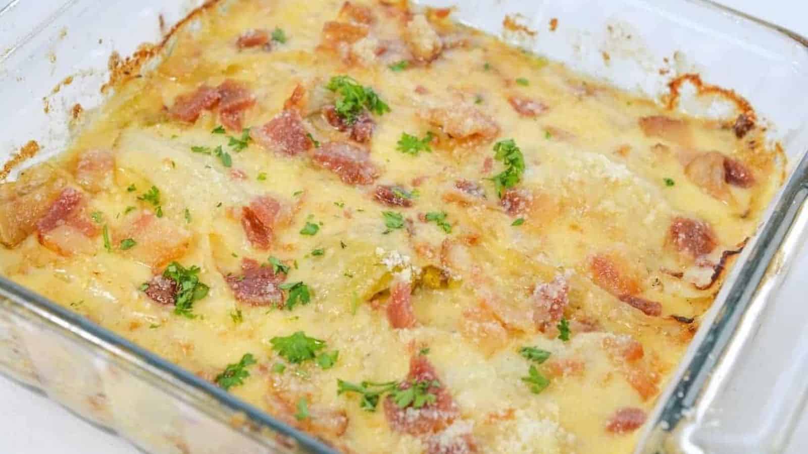 A glass baking dish filled with a creamy, baked casserole. The top is golden brown with visible pieces of crispy bacon, melted cheese, and sprinkled parsley. Edges show slight browning, indicating a well-cooked dish.