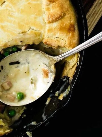 A pot pie with golden-brown crust in a black skillet, partially served.