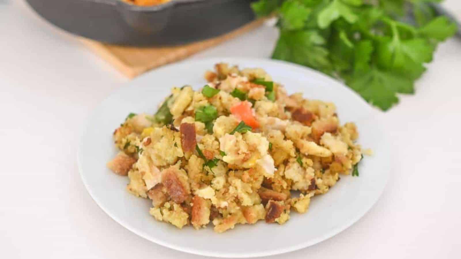 A plate of stuffing with chicken on a table next to a skillet.