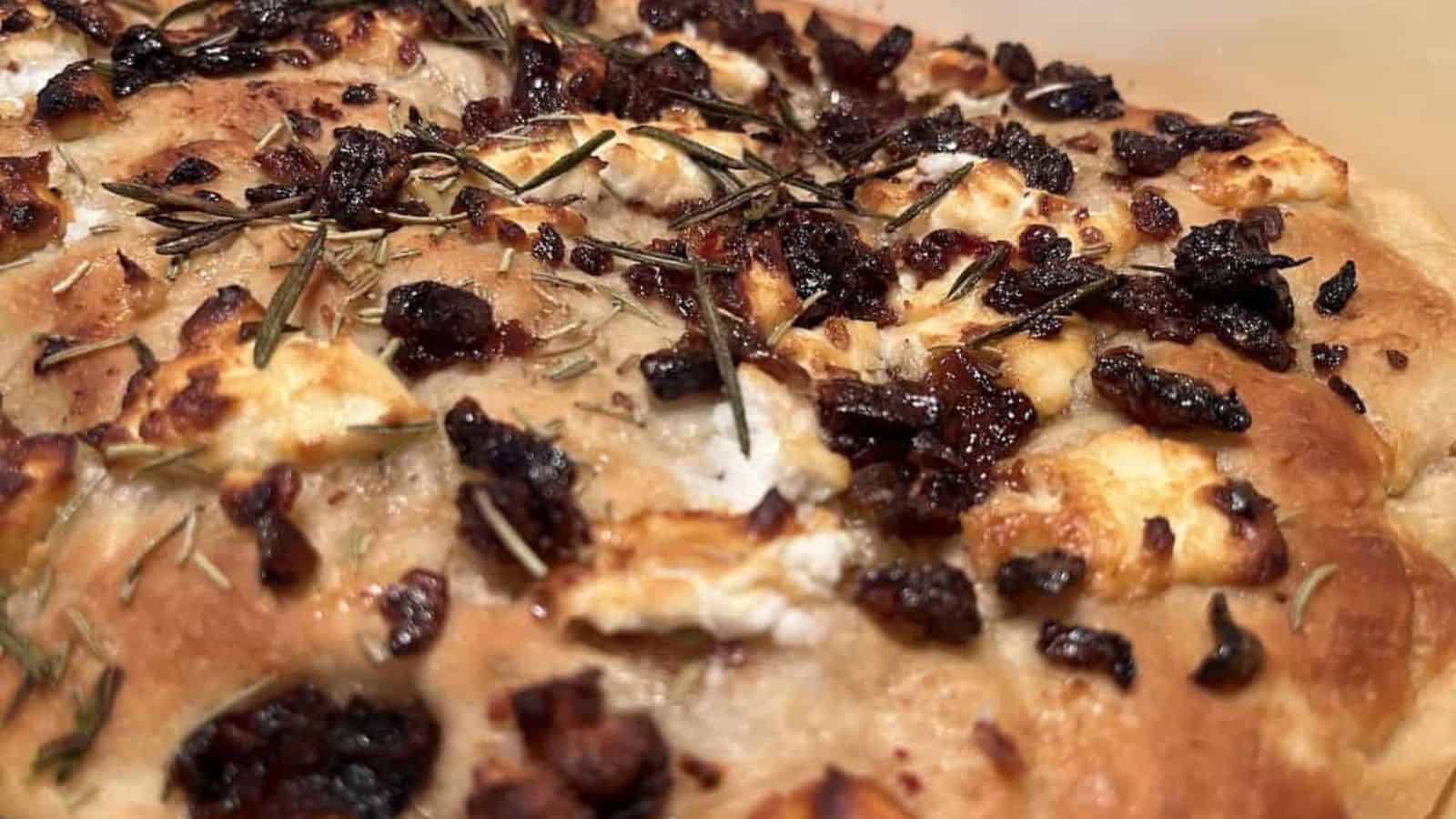 A close-up of freshly baked focaccia topped with rosemary, caramelized onions, and cheese.