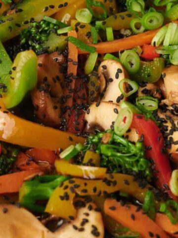 A close-up of a colorful vegetable stir-fry, perfect for the dinner table, featuring broccoli, bell peppers, mushrooms, and sliced green onions. This quick and easy dish is topped with black sesame seeds, highlighting its fresh and vibrant appearance.