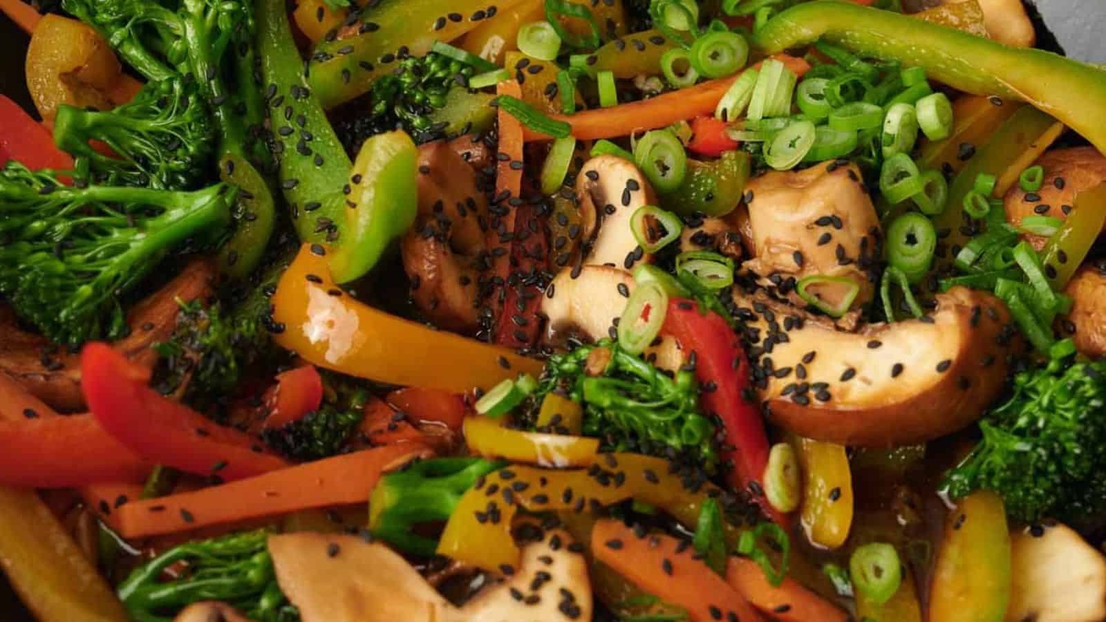 A close-up of a colorful vegetable stir-fry, perfect for the dinner table, featuring broccoli, bell peppers, mushrooms, and sliced green onions. This quick and easy dish is topped with black sesame seeds, highlighting its fresh and vibrant appearance.