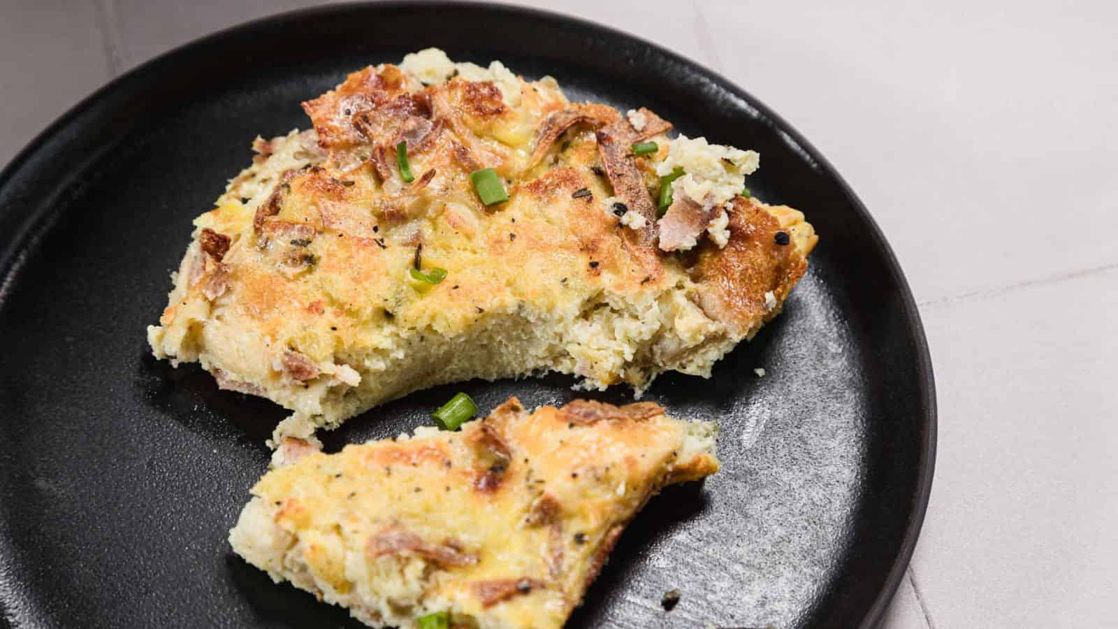 A baked egg and bread casserole in a rectangular metal pan, garnished with chopped green onions. A black and white checkered cloth is partially visible in the background.