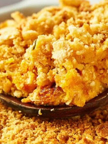 Close-up of a spoon scooping a portion of crumbly, golden-brown topping from a dish. The texture is coarse, suggesting a baked dessert or casserole, with the spoon nestled among the crispy topping.