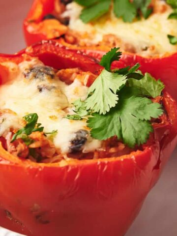Two cooked red bell peppers stuffed with a mixture of rice, mushrooms, and melted cheese, garnished with fresh cilantro, served in a white dish.